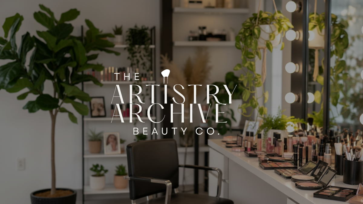 A vanity mirror setup in a beauty salon or makeup station, with cosmetics arranged on the counter, a black salon chair, shelves with products and plants, and large overlaid text reading 'The Artistry Archive Beauty Co.'.