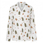 A woman wearing a white long-sleeve pajama shirt with a Christmas-themed print of pine trees, gingerbread cookies, and wrapped gifts, set against a plain white background.