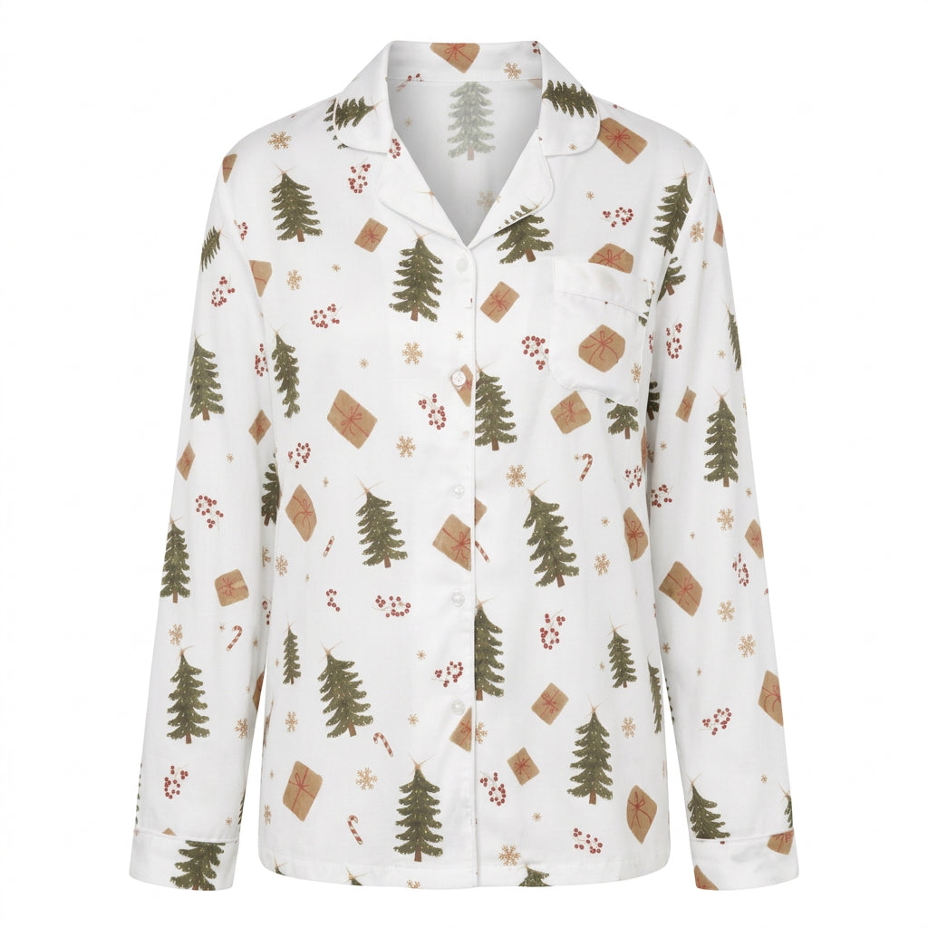 A woman wearing a white long-sleeve pajama shirt with a Christmas-themed print of pine trees, gingerbread cookies, and wrapped gifts, set against a plain white background.