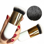 Makeup brush with gold and white handle held by a hand, close-up of bristles shown.