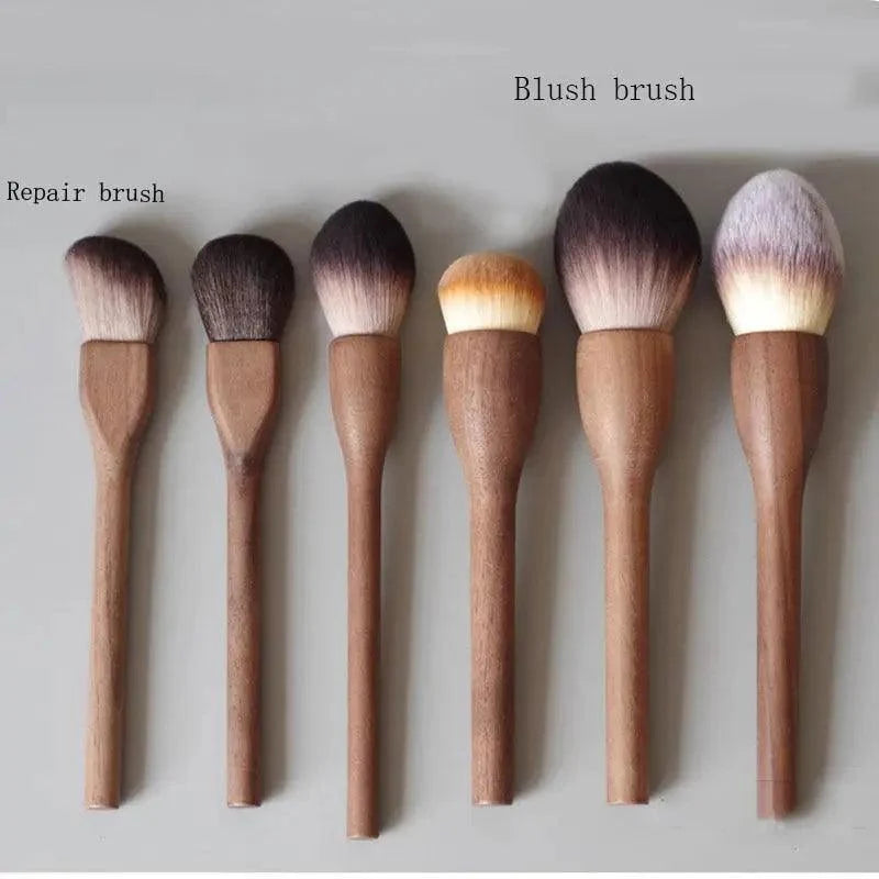 Six makeup brushes with brown wooden handles are arranged in a row on a light gray background. Two brushes on the left are labeled 'Repair brush' and the brush on the far right is labeled 'Blush brush'.
