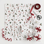 Christmas-themed wrapping paper set with a white background and a festive pattern of red lipsticks, green holly, red bows, candy canes, and stars. The image shows multiple sheets of wrapping paper, some wrapped around gift boxes, along with a roll of red ribbon, scissors, tape, and a tape dispenser on a clean white background.
